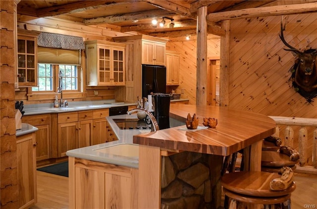 kitchen with light wood-type flooring, a kitchen island, wooden walls, beam ceiling, and black fridge