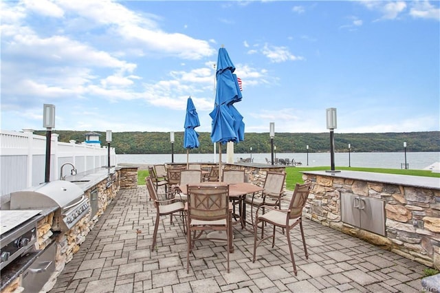 view of patio featuring exterior kitchen, a water view, sink, and a grill