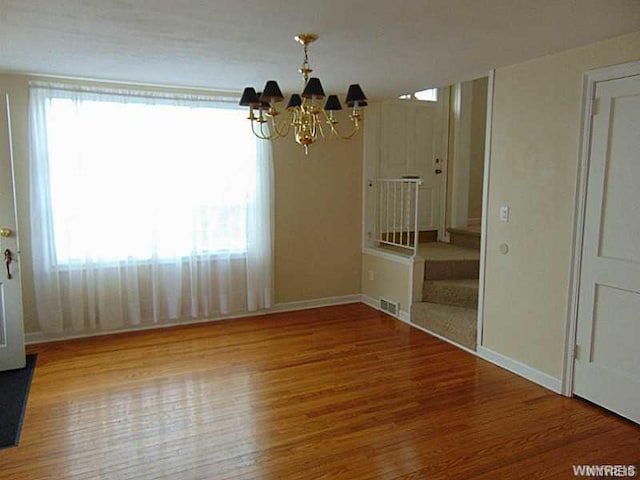 empty room with a healthy amount of sunlight, light hardwood / wood-style floors, and a notable chandelier