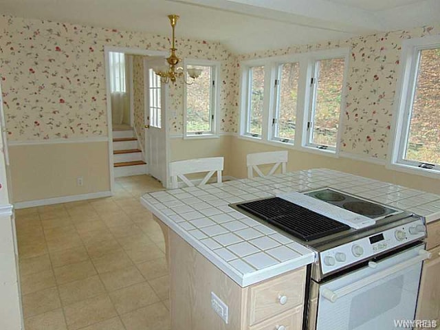 kitchen featuring white range with electric stovetop, an inviting chandelier, a healthy amount of sunlight, and tile counters