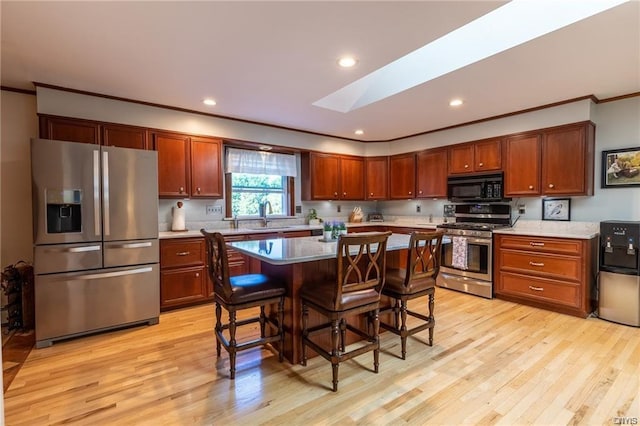 kitchen with a breakfast bar, appliances with stainless steel finishes, a skylight, a kitchen island, and light hardwood / wood-style flooring