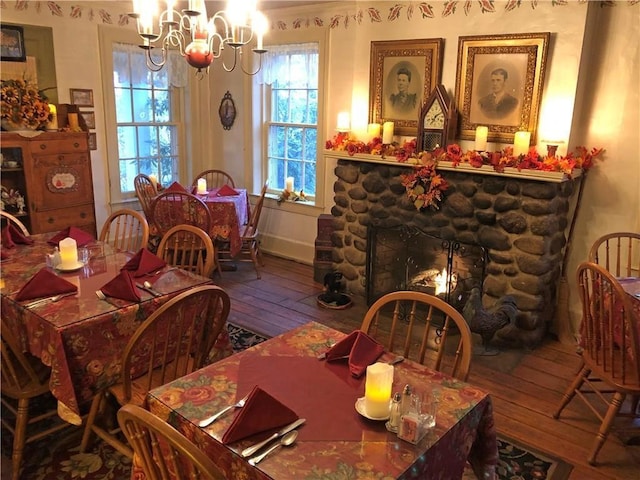 dining space featuring an inviting chandelier, a stone fireplace, and wood-type flooring