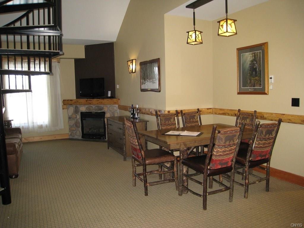 carpeted dining room featuring a stone fireplace and a towering ceiling