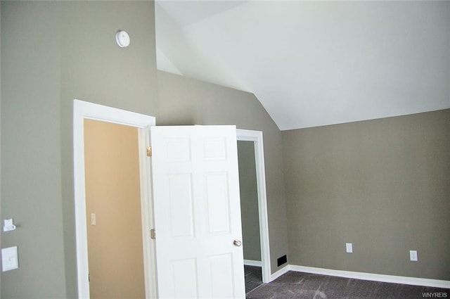 unfurnished bedroom with dark carpet and vaulted ceiling