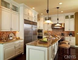 kitchen featuring decorative light fixtures, a kitchen island with sink, wall chimney exhaust hood, and white cabinetry