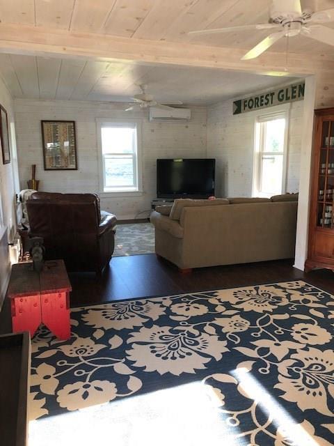 living room with beam ceiling, ceiling fan, dark wood-type flooring, and a wall unit AC