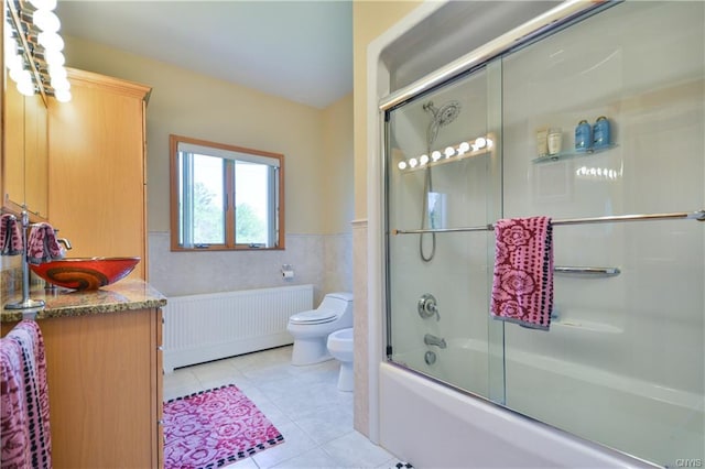 full bathroom featuring toilet, vanity with extensive cabinet space, radiator, tile flooring, and combined bath / shower with glass door