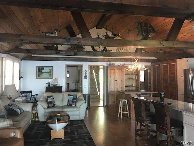 living room featuring plenty of natural light, an inviting chandelier, vaulted ceiling with beams, and dark wood-type flooring