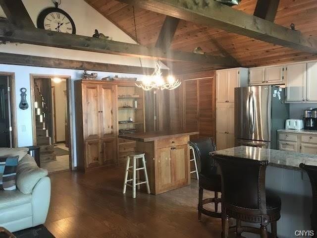 kitchen with a notable chandelier, vaulted ceiling with beams, a center island, stainless steel refrigerator, and dark hardwood / wood-style floors