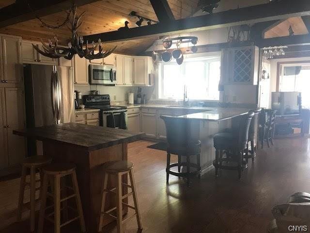 kitchen featuring dark hardwood / wood-style flooring, beamed ceiling, stainless steel appliances, a kitchen bar, and a notable chandelier