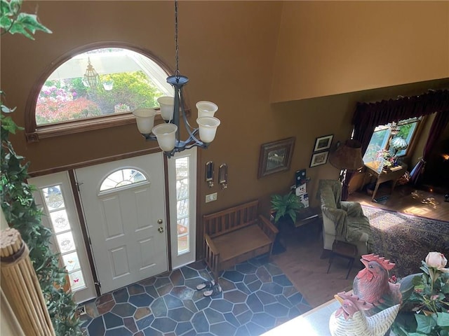 foyer entrance featuring plenty of natural light, dark tile flooring, an inviting chandelier, and a high ceiling