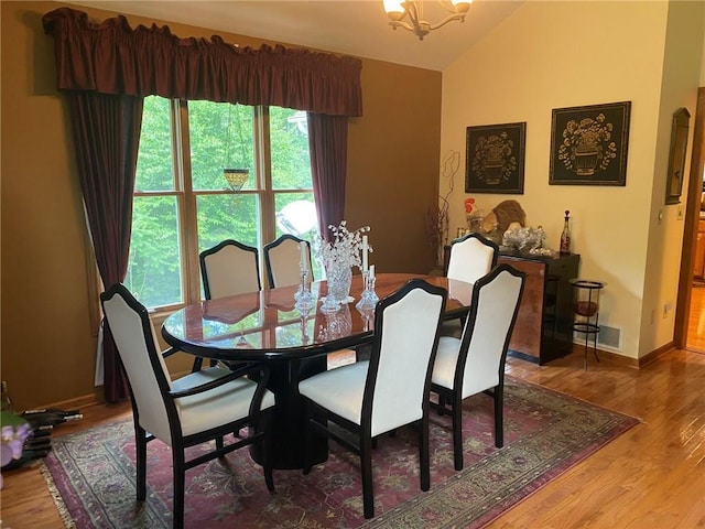 dining area with an inviting chandelier, hardwood / wood-style floors, and vaulted ceiling