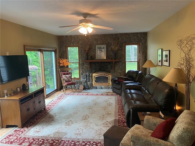 living room featuring ceiling fan, a wealth of natural light, and a stone fireplace