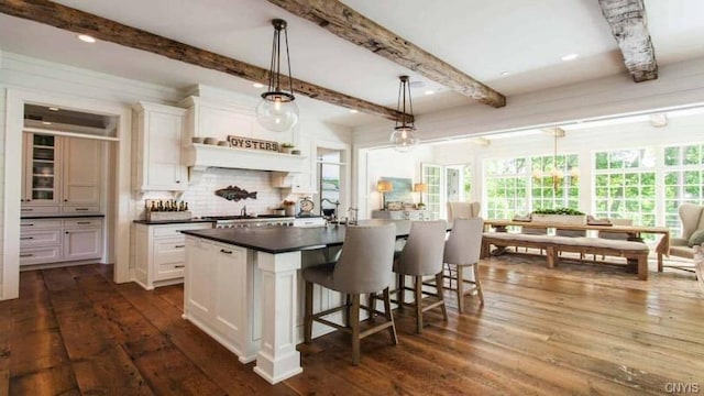 kitchen with dark hardwood / wood-style flooring, white cabinetry, beamed ceiling, and a center island with sink