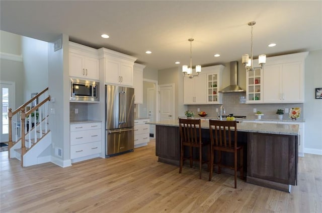 kitchen featuring wall chimney exhaust hood, tasteful backsplash, stainless steel appliances, and light wood-type flooring