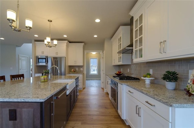 kitchen featuring appliances with stainless steel finishes, hanging light fixtures, tasteful backsplash, and light hardwood / wood-style flooring