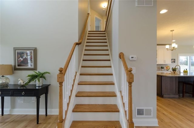 staircase featuring a chandelier, sink, and light wood-type flooring