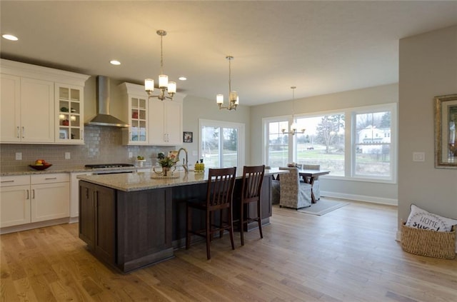 kitchen featuring wall chimney range hood, light hardwood / wood-style floors, and a chandelier