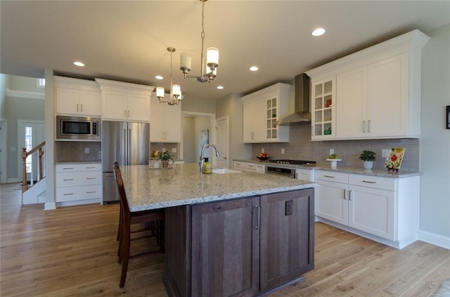 kitchen featuring light hardwood / wood-style floors, a chandelier, stainless steel appliances, and wall chimney exhaust hood