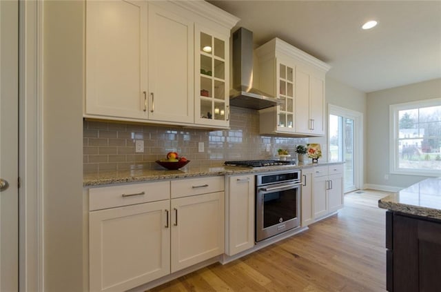 kitchen featuring light hardwood / wood-style flooring, stainless steel appliances, wall chimney range hood, and white cabinets