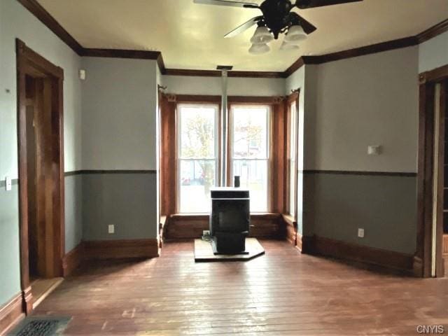 spare room featuring ornamental molding, ceiling fan, dark wood-type flooring, and a wood stove