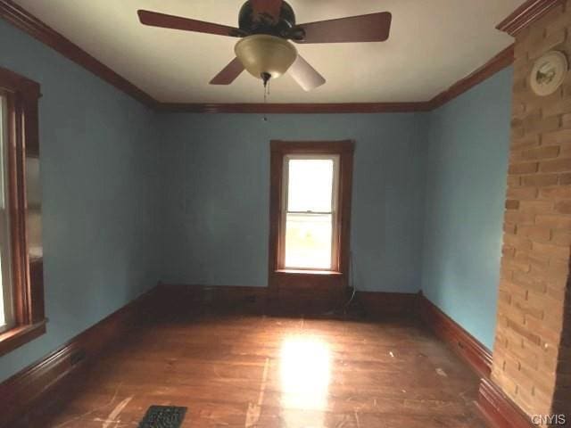 spare room with ceiling fan, brick wall, dark wood-type flooring, and ornamental molding