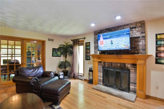 living room with a healthy amount of sunlight, a fireplace, brick wall, light hardwood / wood-style floors, and baseboard heating