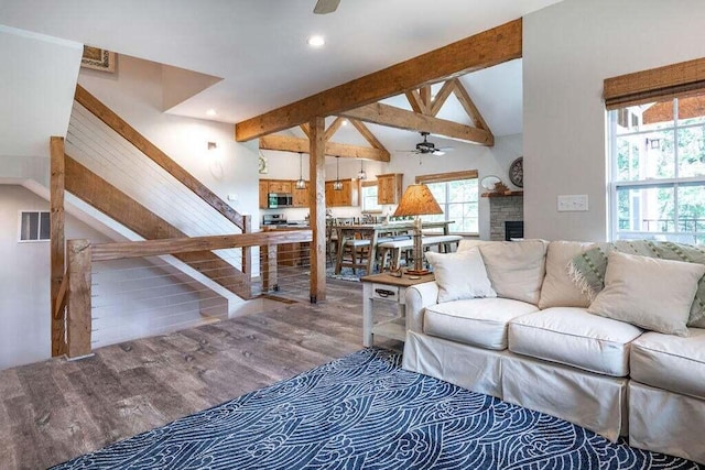 living room with beamed ceiling, ceiling fan, high vaulted ceiling, a stone fireplace, and hardwood / wood-style flooring