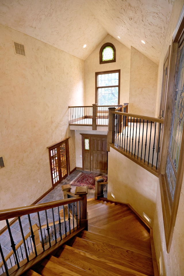 stairway with hardwood / wood-style floors and high vaulted ceiling