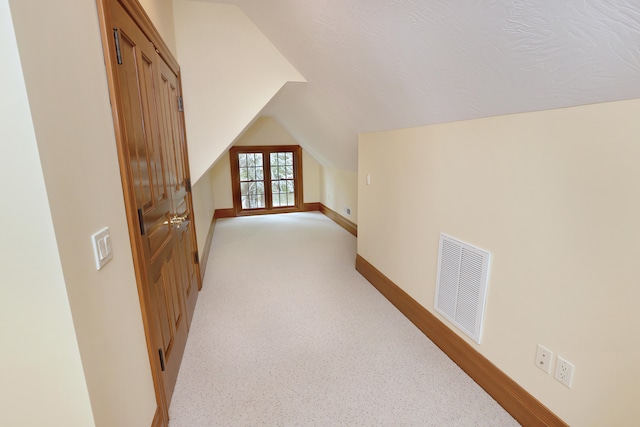 additional living space with light carpet, french doors, vaulted ceiling, and a textured ceiling