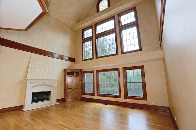 unfurnished living room with light wood-type flooring and a towering ceiling