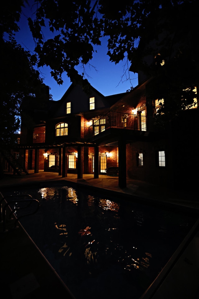 back house at twilight featuring a balcony and a patio area