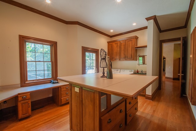 kitchen featuring ornamental molding, a kitchen island, built in desk, washing machine and dryer, and light hardwood / wood-style floors