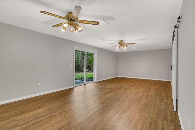 empty room with ceiling fan, a textured ceiling, light wood-type flooring, and a barn door