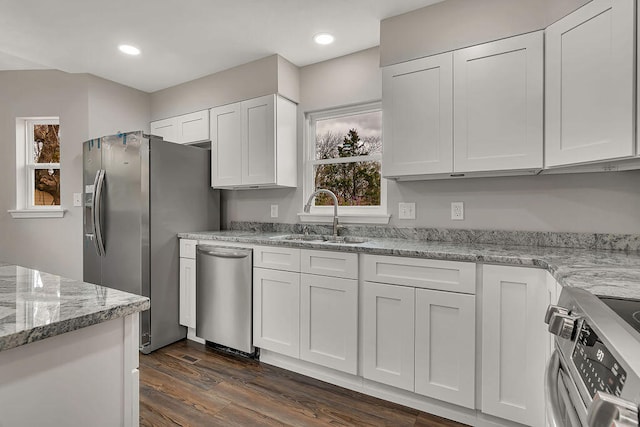 kitchen with light stone countertops, white cabinets, dark wood-type flooring, sink, and appliances with stainless steel finishes