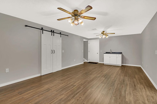 interior space featuring ceiling fan, a barn door, sink, and dark hardwood / wood-style flooring