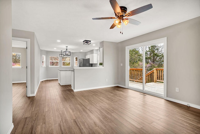 unfurnished living room with ceiling fan with notable chandelier, a healthy amount of sunlight, and wood-type flooring