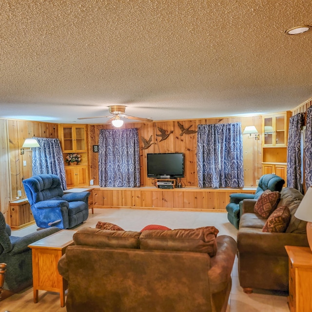 living room featuring ceiling fan, a textured ceiling, and wooden walls