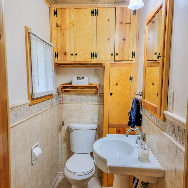 bathroom featuring toilet, a wainscoted wall, a sink, and tile walls