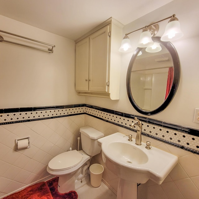 half bath with tile patterned flooring, toilet, a wainscoted wall, and tile walls