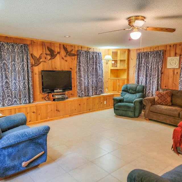 living room featuring ceiling fan, wood walls, and a textured ceiling