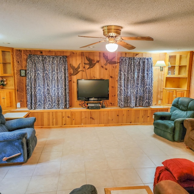 tiled living room with ceiling fan, a textured ceiling, wooden walls, and built in shelves