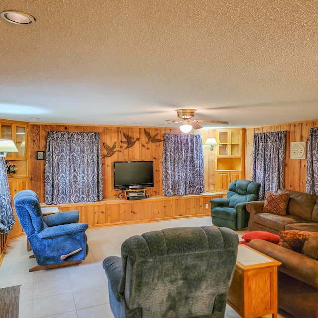 living room featuring ceiling fan, a textured ceiling, and wood walls