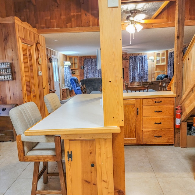 kitchen with ceiling fan, wooden walls, light tile patterned floors, and kitchen peninsula