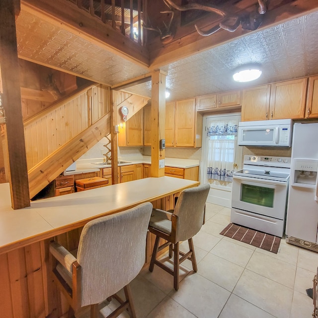 kitchen with light tile patterned flooring, wooden walls, white appliances, and a breakfast bar area