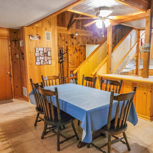 tiled dining area featuring ceiling fan, a textured ceiling, and wood walls