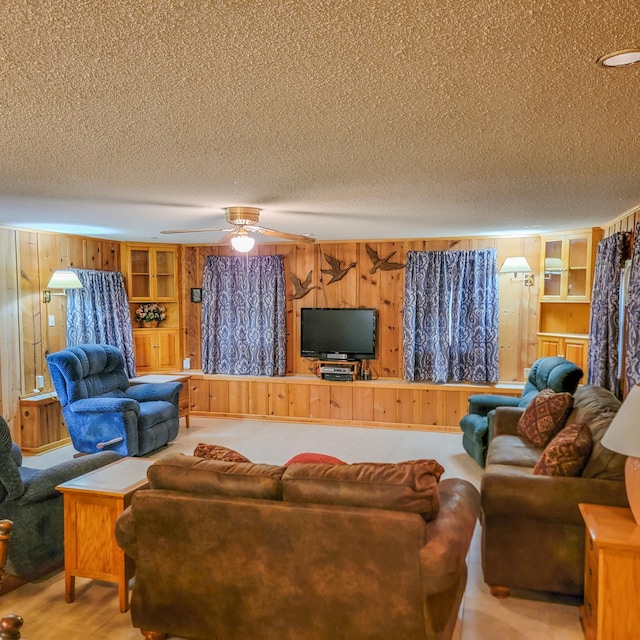 living room with ceiling fan, a textured ceiling, wooden walls, and built in features