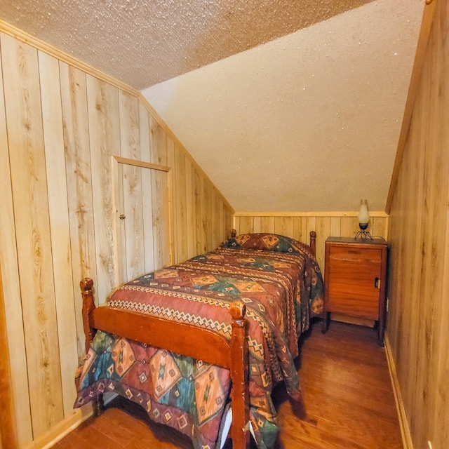 bedroom featuring hardwood / wood-style floors, vaulted ceiling, wooden walls, and a textured ceiling