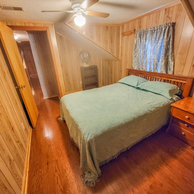 bedroom featuring ceiling fan, wood walls, hardwood / wood-style floors, and a textured ceiling