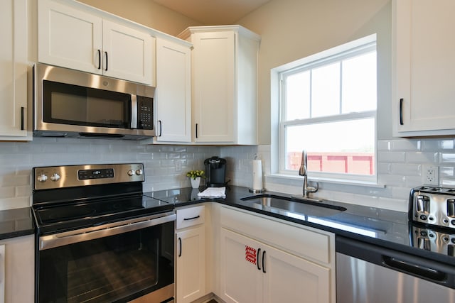 kitchen featuring white cabinets, sink, backsplash, appliances with stainless steel finishes, and dark stone countertops